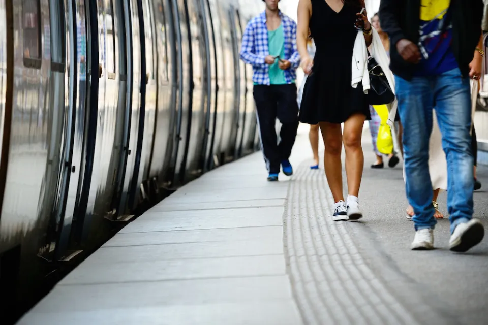 Low shot of side of subway or commuter train and passengers walking on platform next to it.